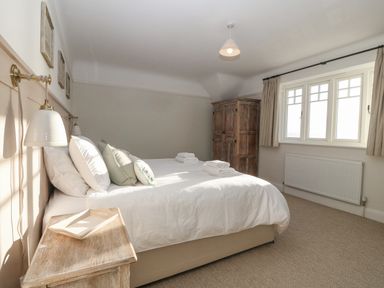 A bedroom with a bed pillows bedside table wooden wardrobe and window with curtains at Haul A Gwynt in Criccieth