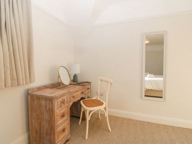 A wooden desk with a mirror and lamp next to a chair and a wall mirror in a room at Haul A Gwynt in Criccieth