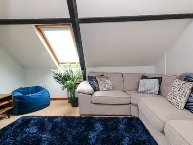 A living room with a beige sectional sofa with pillows a blue bean bag a plant under a skylight window and a blue shaggy rug at Horseshoe Cottage in Hartland