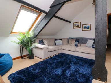 A corner sofa with cushions near slanted ceiling window and black beams in a living room at Horseshoe Cottage in Hartland
