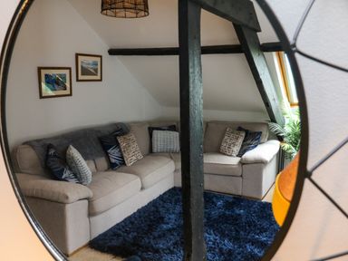 A living room with a beige sectional sofa with cushions a blue rug framed pictures on the wall and wooden beams at Horseshoe Cottage in Hartland