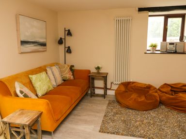 A sitting area with an orange sofa with cushions bean bags a side table and a window at Horseshoe Cottage in Hartland