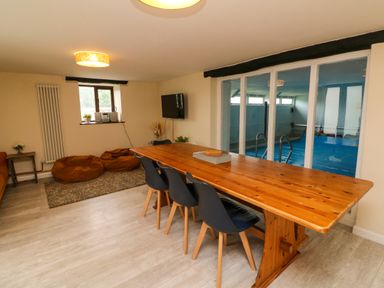 A dining area with a wooden table and black chairs next to glass doors overlooking an indoor pool at Horseshoe Cottage in Hartland