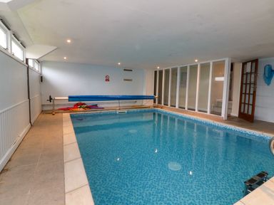 An indoor swimming pool with tiled floor and a pool cover roller at Horseshoe Cottage in Hartland