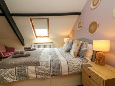 A bedroom with a double bed patterned bedding bedside table with lamp and folded towels at Horseshoe Cottage in Hartland