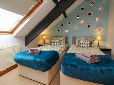 A bedroom with two single beds side by side with blue blankets and towels on top at Horseshoe Cottage in Hartland