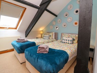 A bedroom with two single beds blue throws and round mirrors on a blue wall at Horseshoe Cottage in Hartland