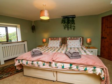 A bedroom with a double bed with floral bedding towels on the bed bedside tables with lamps a window a door and plants at Horseshoe Cottage in Hartland