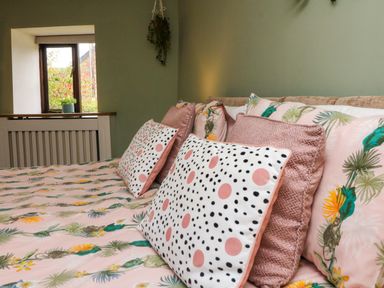 A bed with patterned pillows and floral bedding near a window with a small plant at Horseshoe Cottage in Hartland