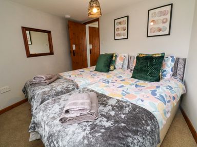 A bedroom with two single beds with colorful bedding and green cushions at Horseshoe Cottage in Hartland