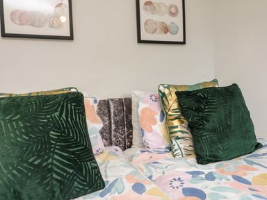A bed with patterned pillows and floral bed sheets under two framed pictures on a wall at Horseshoe Cottage in Hartland
