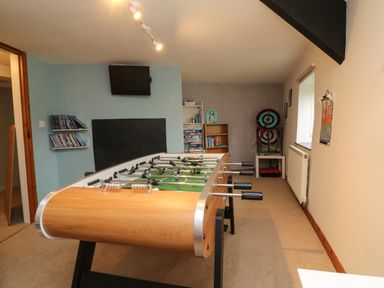 A game room with a foosball table a TV shelf with DVDs a bookshelf with board games and dartboards at Horseshoe Cottage in Hartland