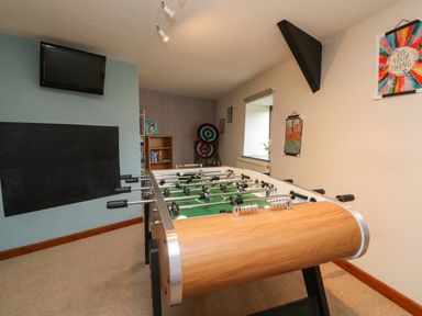 A game room with a foosball table a wall-mounted tv a bookcase and dart boards at Horseshoe Cottage in Hartland