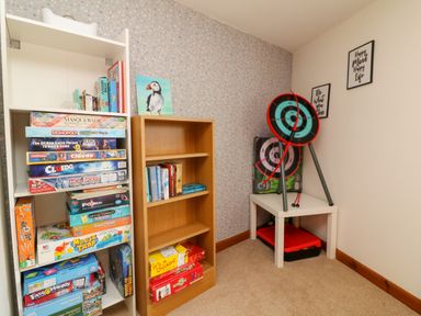 A room corner with shelves of board games and books and a table holding a dartboard at Horseshoe Cottage in Hartland