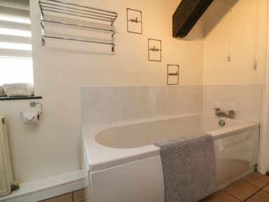 A bathroom with a bathtub with a towel hanging on it and a towel rack on the wall at Horseshoe Cottage in Hartland