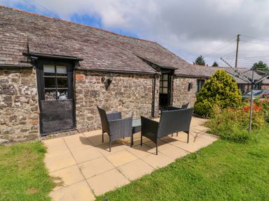 An outdoor seating area with a table and four chairs on a patio beside a stone cottage with a sloped roof at Horseshoe Cottage in Hartland