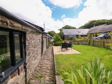 A stone wall cottage with a patio table and chairs on a lawn surrounded by a wooden fence at Horseshoe Cottage in Hartland