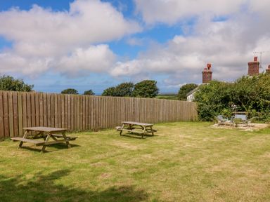 A grassy backyard with two wooden picnic tables and a seating area with metal chairs at Horseshoe Cottage in Hartland