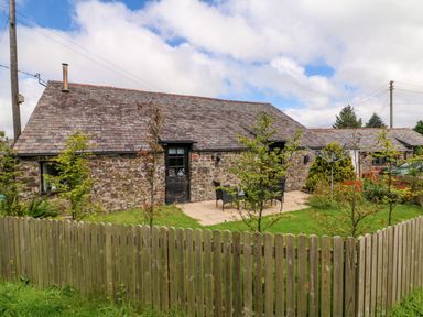 A stone cottage with a slate roof and a fenced garden with patio furniture and small trees at Horseshoe Cottage in Hartland