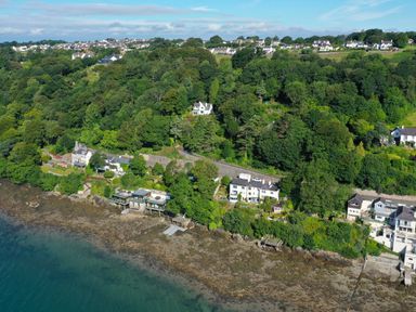 A coastal area with houses along the shoreline and dense trees behind at Afallon Menai Bridge