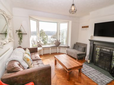 A living room with a brown sofa a wooden coffee table a built in window seat and a fireplace at Afallon in Menai Bridge