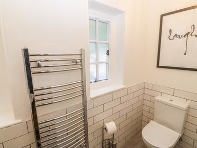 A bathroom with a toilet a chrome towel radiator a roll of toilet paper and a framed print on the wall at Afallon in Menai Bridge