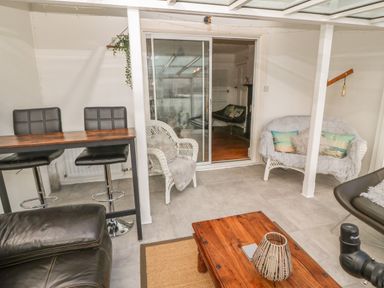 A seating area with bar stools a wooden table white wicker chairs and sliding glass doors at Afallon Menai Bridge