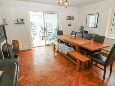 A dining room with a wooden table, black chairs, a bench with a fur throw, a fireplace, a sliding glass door, and wall decorations at Afallon in Menai Bridge