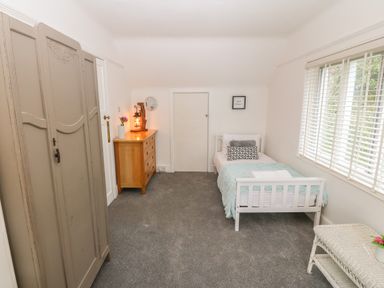 A bedroom with a single white bed a wooden dresser a grey wardrobe and a window with blinds at Afallon in Menai Bridge