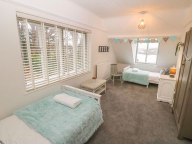 A bedroom with two single beds a small table a chair a window and carpeted floor at Afallon in Menai Bridge