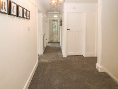 A hallway with grey carpet multiple white doors framed letters on the wall spelling relax at Afallon in Menai Bridge