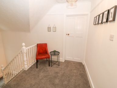 A hallway with a red chair beside a small black round table and white door at Afallon in Menai Bridge