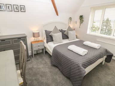 A bedroom with a double bed grey bedding and pillows bedside tables lamps a chest of drawers a desk and chair with window blinds and hanging plants at Afallon in Menai Bridge