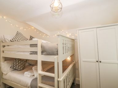 A bedroom with a white bunk bed decorated with gray and white pillows and a white wardrobe at Afallon in Menai Bridge