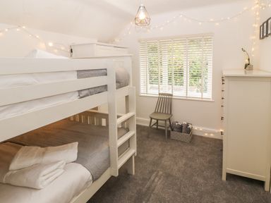 A bedroom with a white bunk bed a green chair a white dresser and string lights at Afallon in Menai Bridge