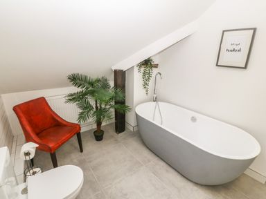 A bathroom with a freestanding bathtub a red chair a potted plant and a framed print on the wall at Afallon in Menai Bridge