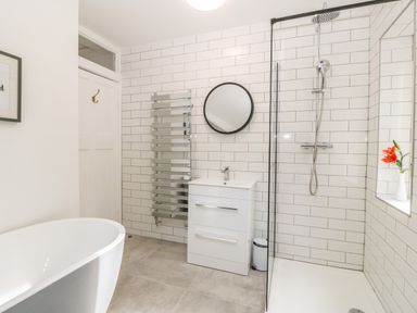 A bathroom with a freestanding bathtub a shower with glass partition a white vanity unit and a round mirror at Afallon Menai Bridge