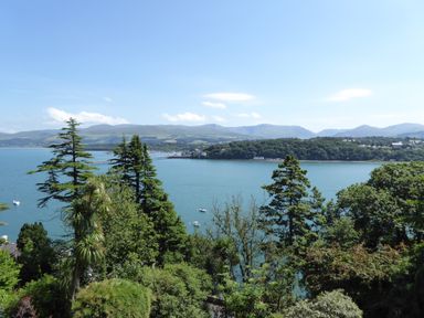 A view of a bay with trees in the foreground and mountains in the background at Afallon in Menai Bridge