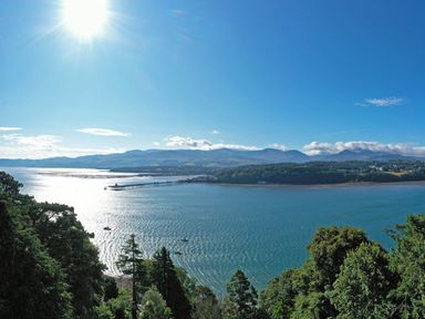 A coastal view with a pier extending into the water trees in the foreground and mountains in the background at Afallon Menai Bridge
