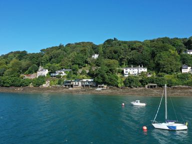 A waterfront with several houses on a forested hillside and boats on the water at Afallon Menai Bridge