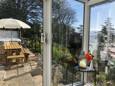 A glass door opening to a patio with a wooden picnic table umbrella and garden statues at Afallon in Menai Bridge