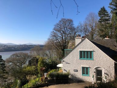 A white house with blue window frames surrounded by trees and overlooking a river at Afallon in Menai Bridge