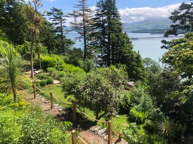 A garden with trees shrubs and a rope fence overlooking the sea and a pier at Afallon in Menai Bridge