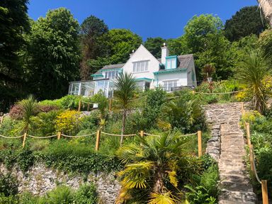 A white house with blue trim on a hill surrounded by greenery and stone steps at Afallon in Menai Bridge