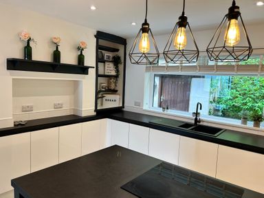 A kitchen with black countertops white cabinets hanging lights and a window with plants at Afallon Menai Bridge