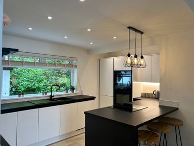 A kitchen with black countertops white cabinets an island with stools and hanging lights at Afallon in Menai Bridge