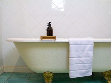 A bathtub with a bottle on a shelf and a towel at Carrows Stable in Morwenstow