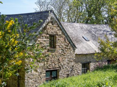 A stone building with a sloped roof and windows at Carrows Stable in Morwenstow