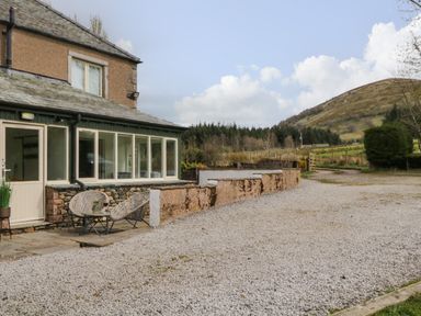 A gravel driveway beside a house with outdoor chairs and a table near a countryside hill at Glen Cottage in Troutbeck near Keswick