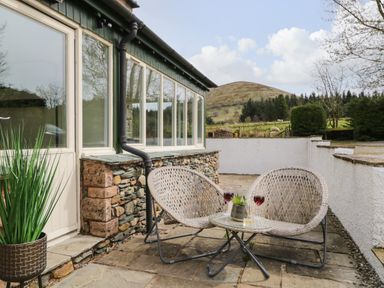 A patio with two woven chairs and a small round table with drinks outside a house at Glen Cottage in Troutbeck near Keswick
